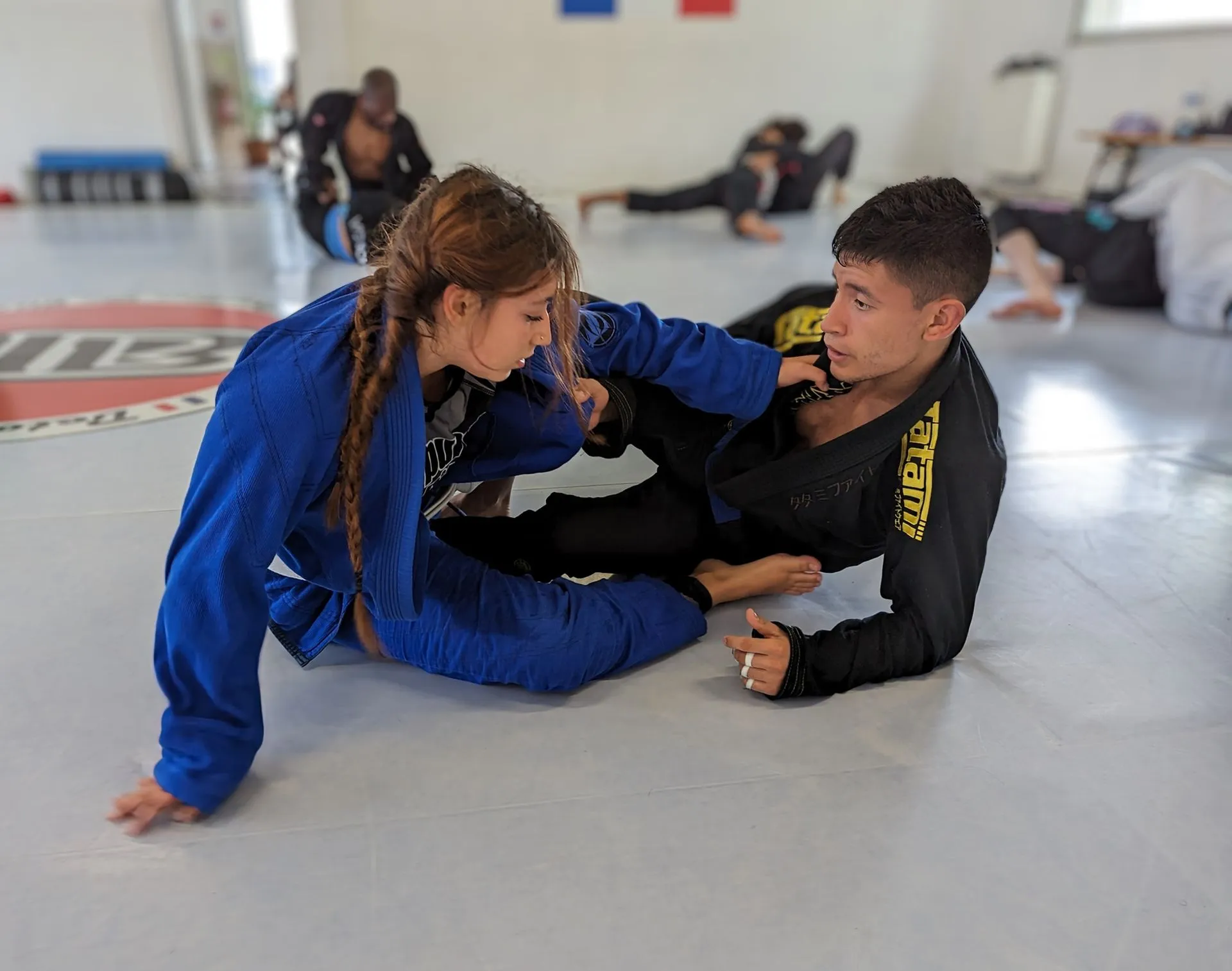 Deux pratiquants en kimono travaillent la garde au sol, sur le tapis du club