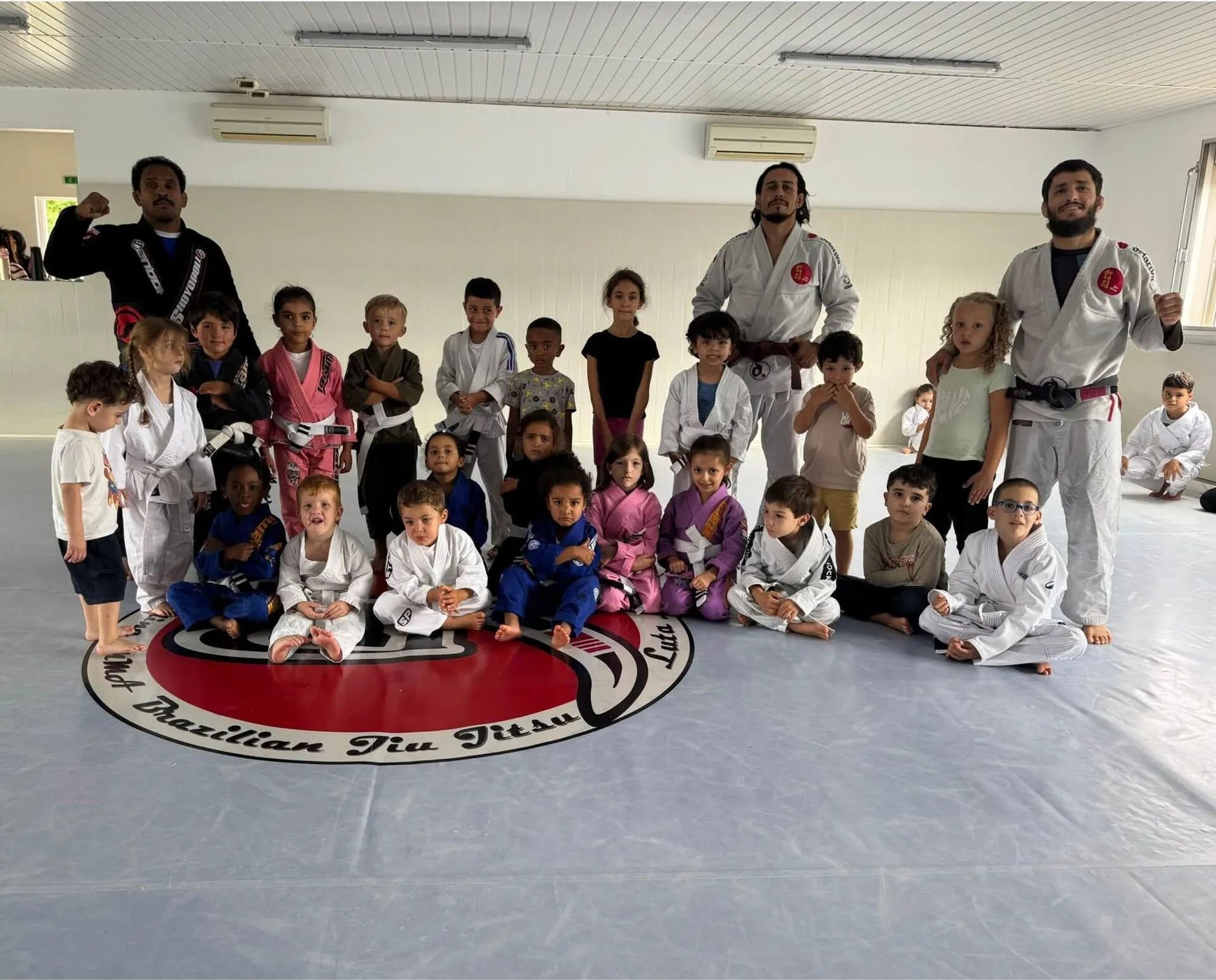 Les enfants du club en kimono, assis en groupe autour de l’emblème peint sur le tapis